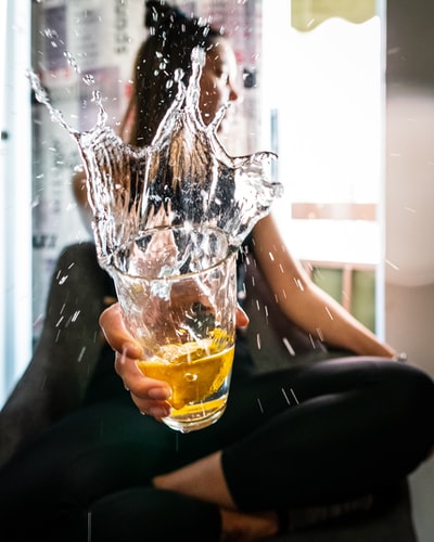 把黄色液体倒在透明玻璃杯上的人
